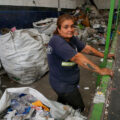 Gabriela Villalba posa junto a una cinta transportadora que antes se utilizaba para clasificar materiales reciclables en la planta de reciclaje de la cooperativa Construyendo Desde Abajo en La Matanza. Al igual que muchas cooperativas en Argentina, esta enfrenta dificultades debido a la caída de los precios de los materiales y a la reducción de la fuerza laboral, lo que provoca que más reciclables terminen en vertederos. Foto: Lucila Pellettieri

