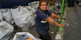 Gabriela Villalba posa junto a una cinta transportadora que antes se utilizaba para clasificar materiales reciclables en la planta de reciclaje de la cooperativa Construyendo Desde Abajo en La Matanza. Al igual que muchas cooperativas en Argentina, esta enfrenta dificultades debido a la caída de los precios de los materiales y a la reducción de la fuerza laboral, lo que provoca que más reciclables terminen en vertederos. Foto: Lucila Pellettieri

